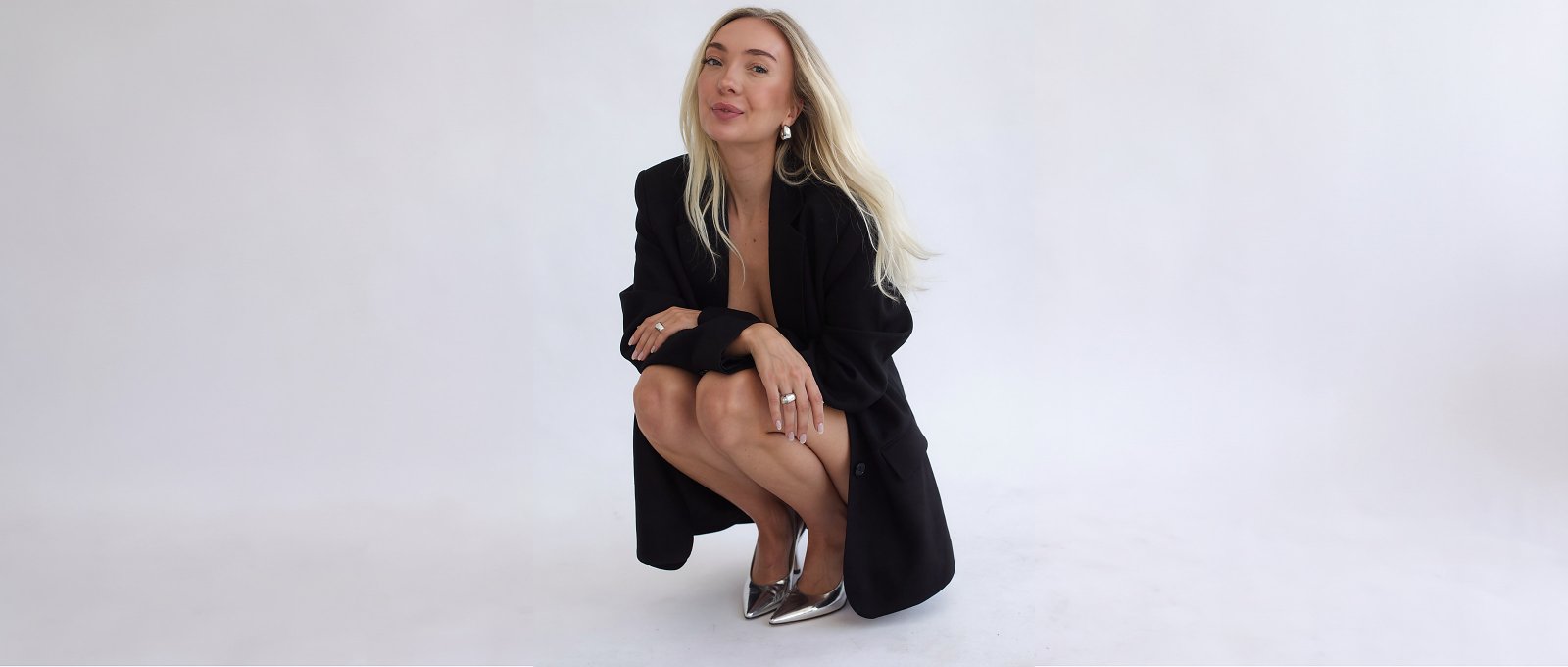 Elle in schwarzem Blazer, hockend vor weißem Studiohintergrund
